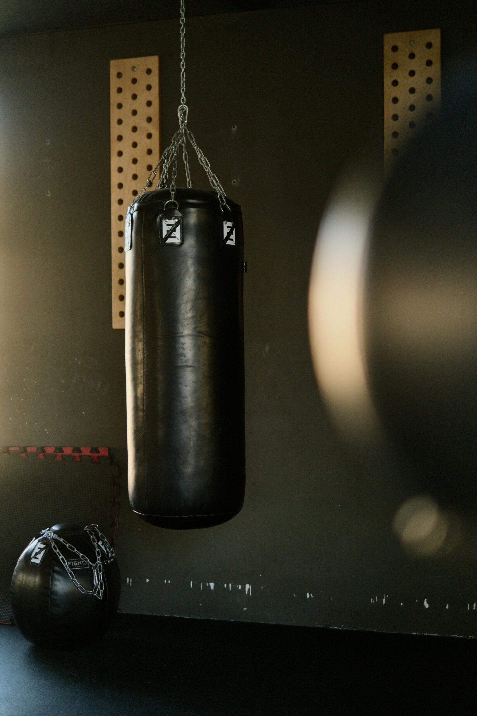 Black punching bag hangs in a gym, bathed in sunlight, creating a moody and focused atmosphere.